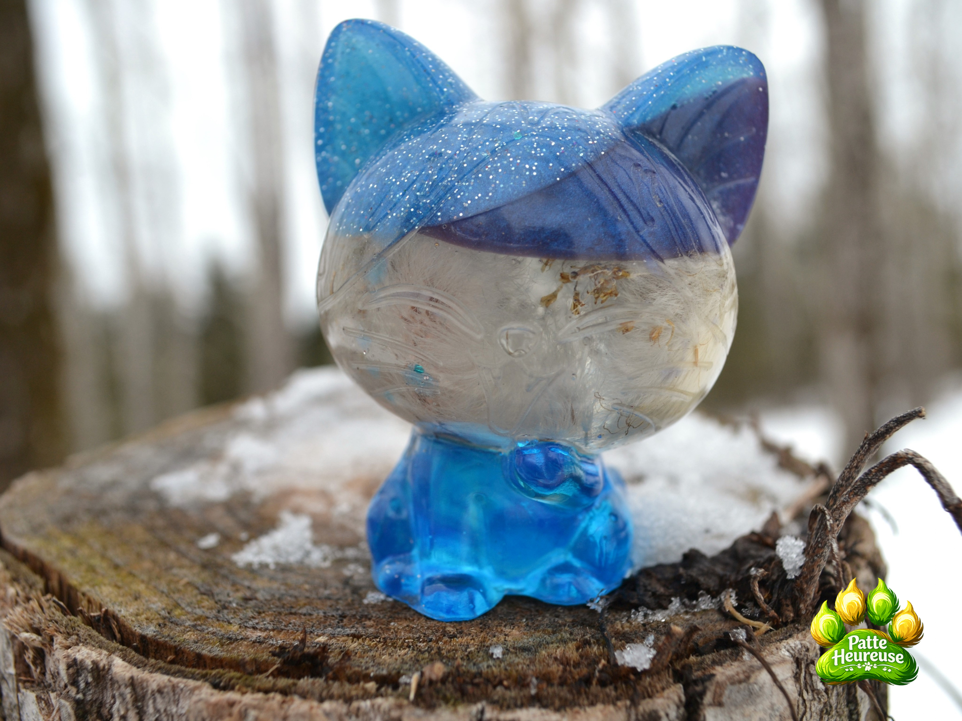 petit chat translucide bleu brillant sur un tronc d'arbre enneigé 